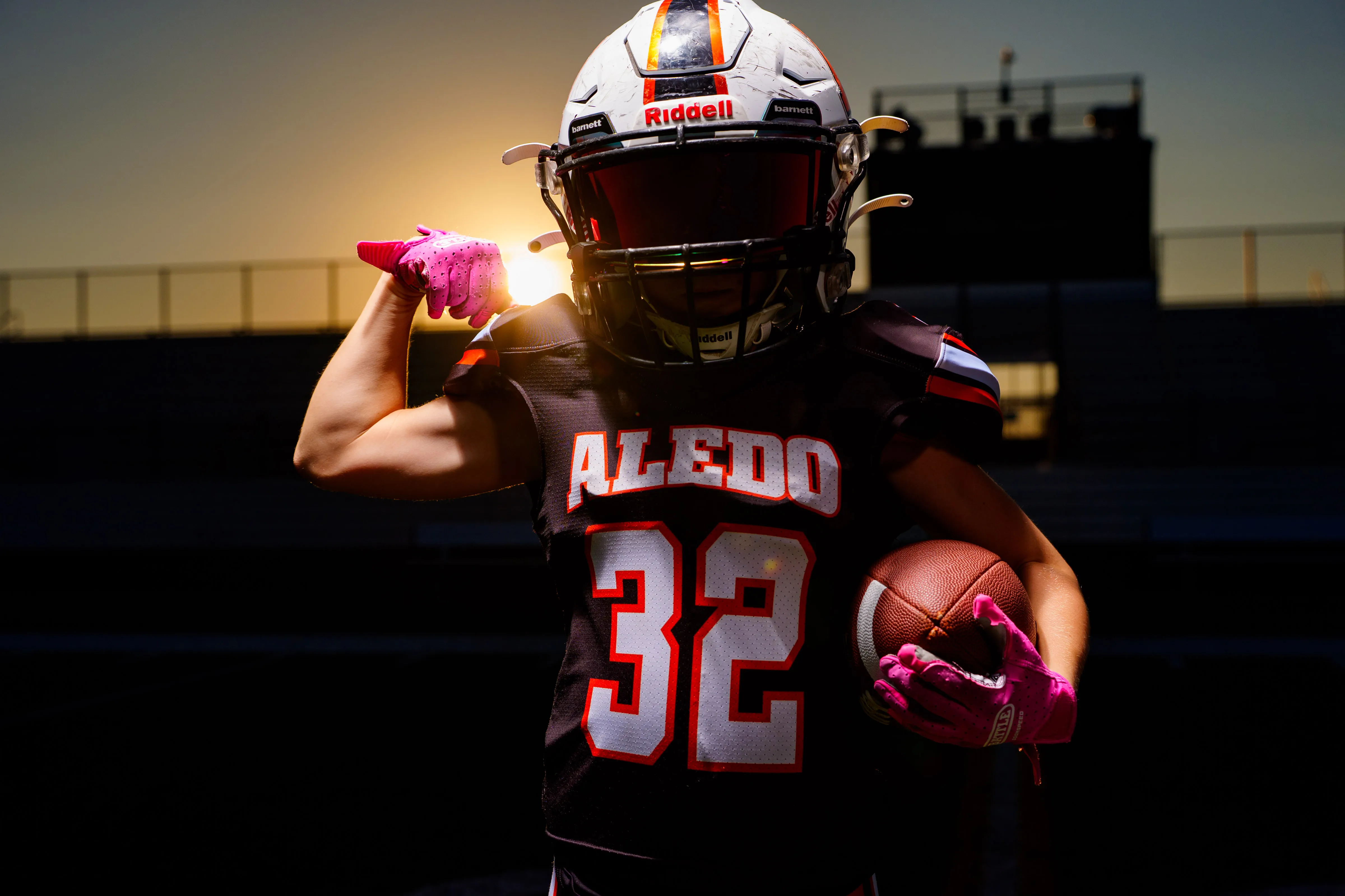 Youth football player flexing in uniform at sunset on the stadium field