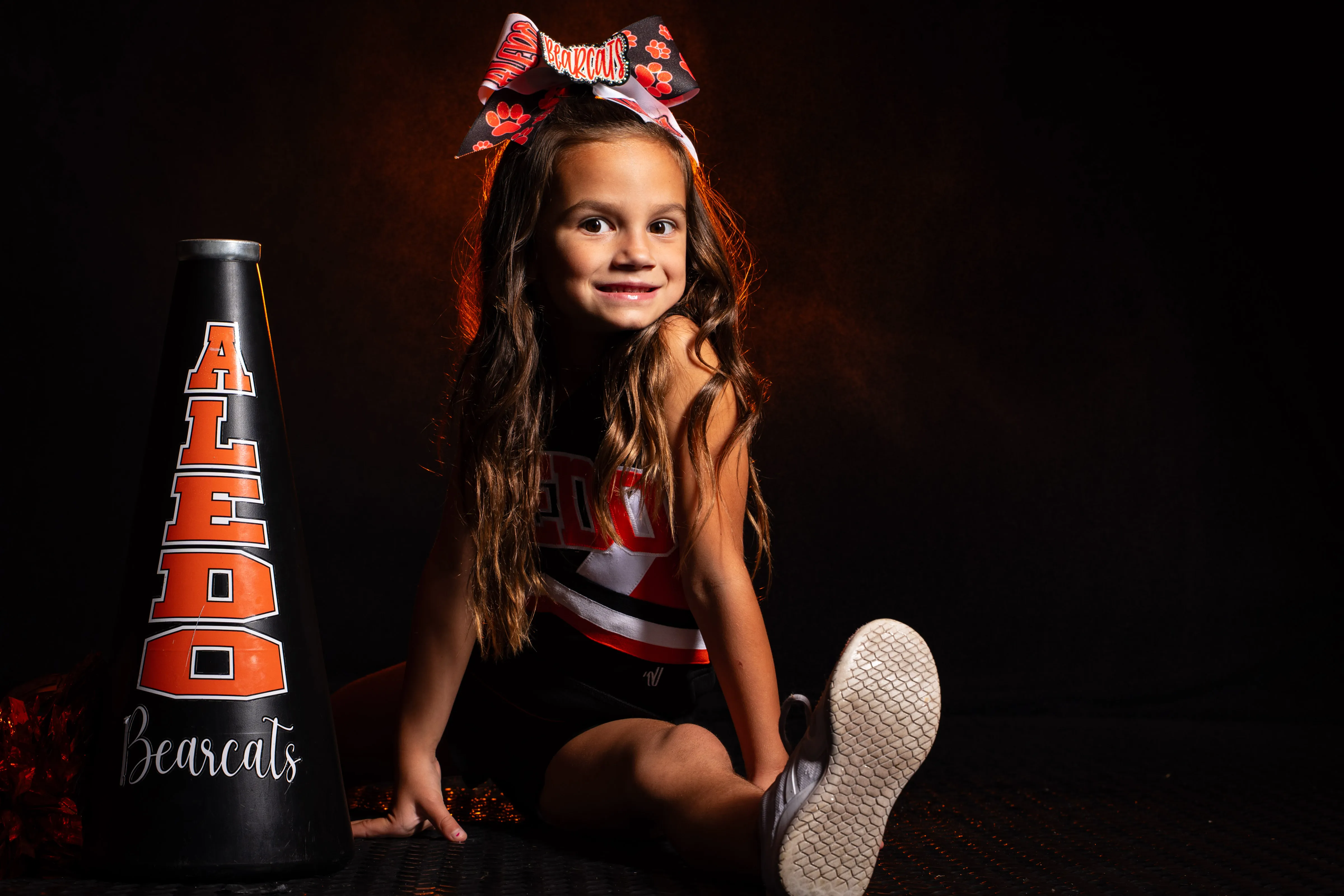 Young cheerleader in Aledo uniform posing with a megaphone, studio portrait