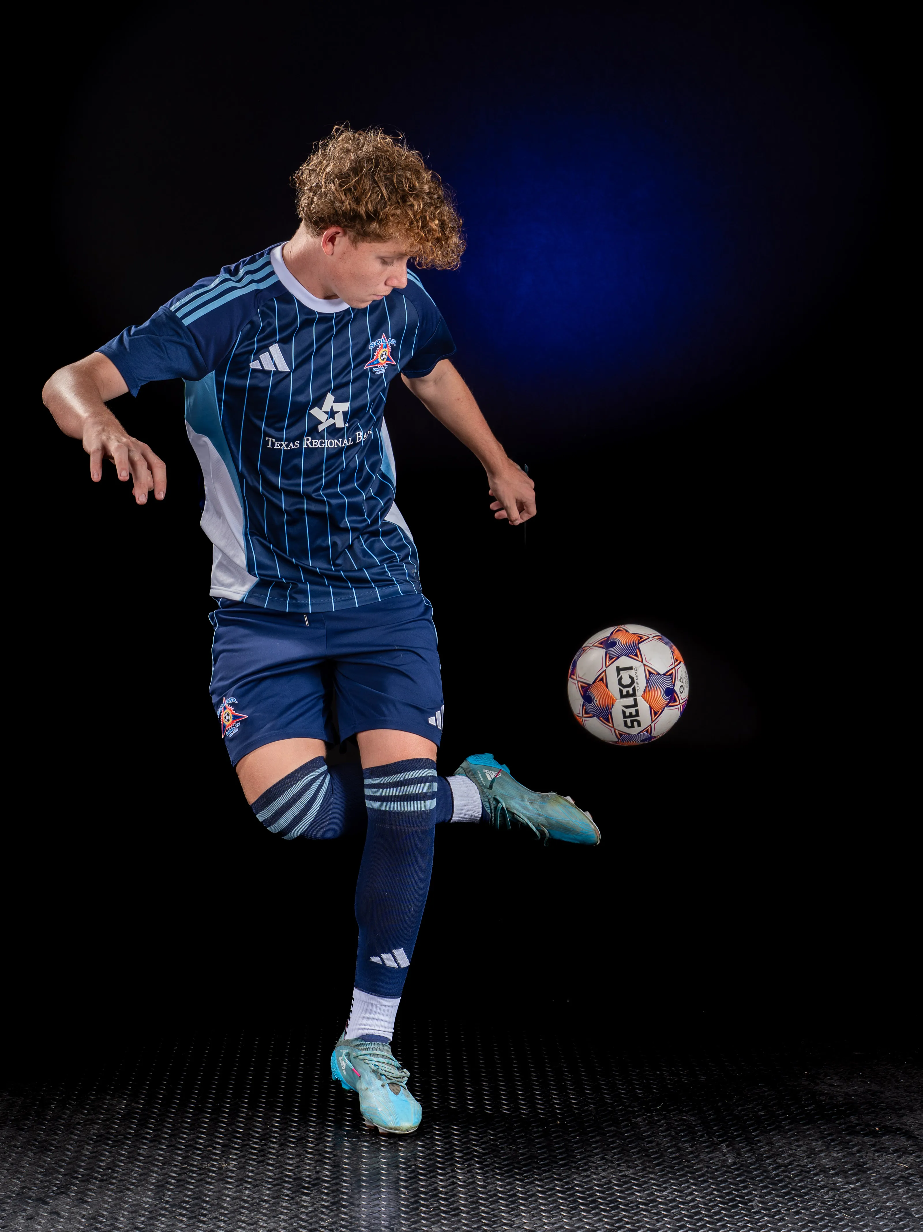 Soccer player juggling the ball, studio sports portrait on black