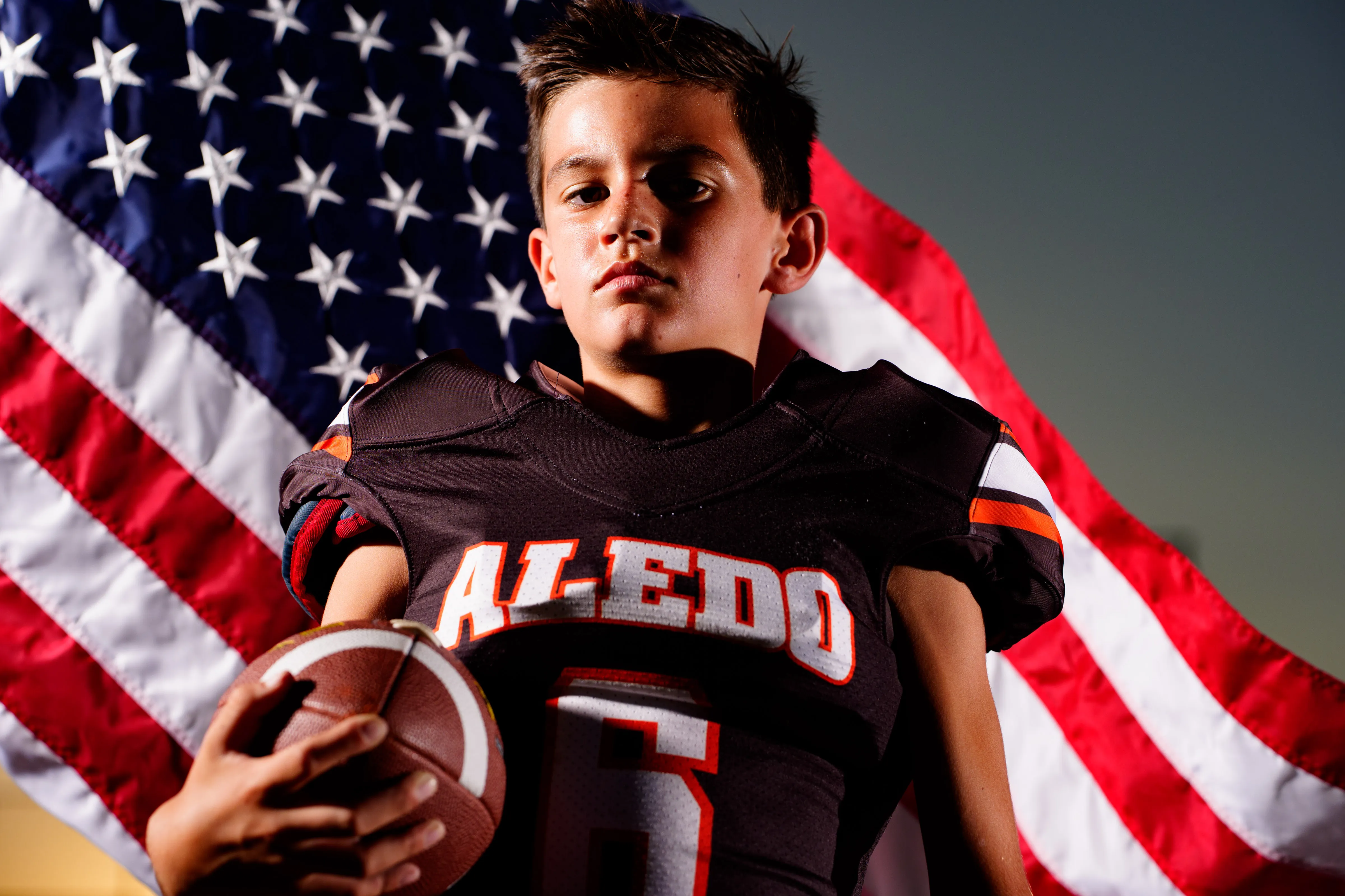 Youth football player holding a football with the American flag, studio portrait