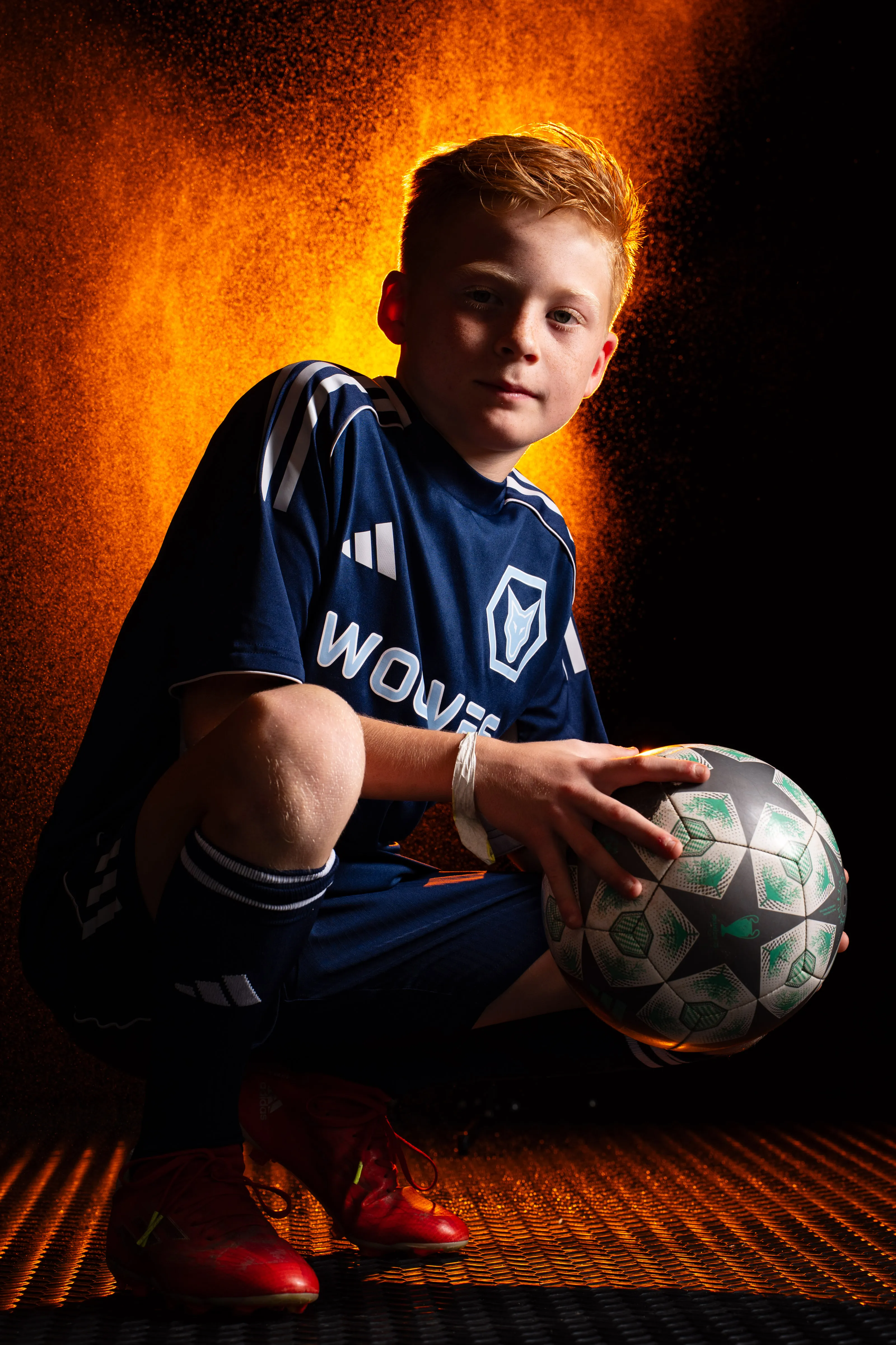 Soccer player crouched with the ball, backlit by an orange powder burst