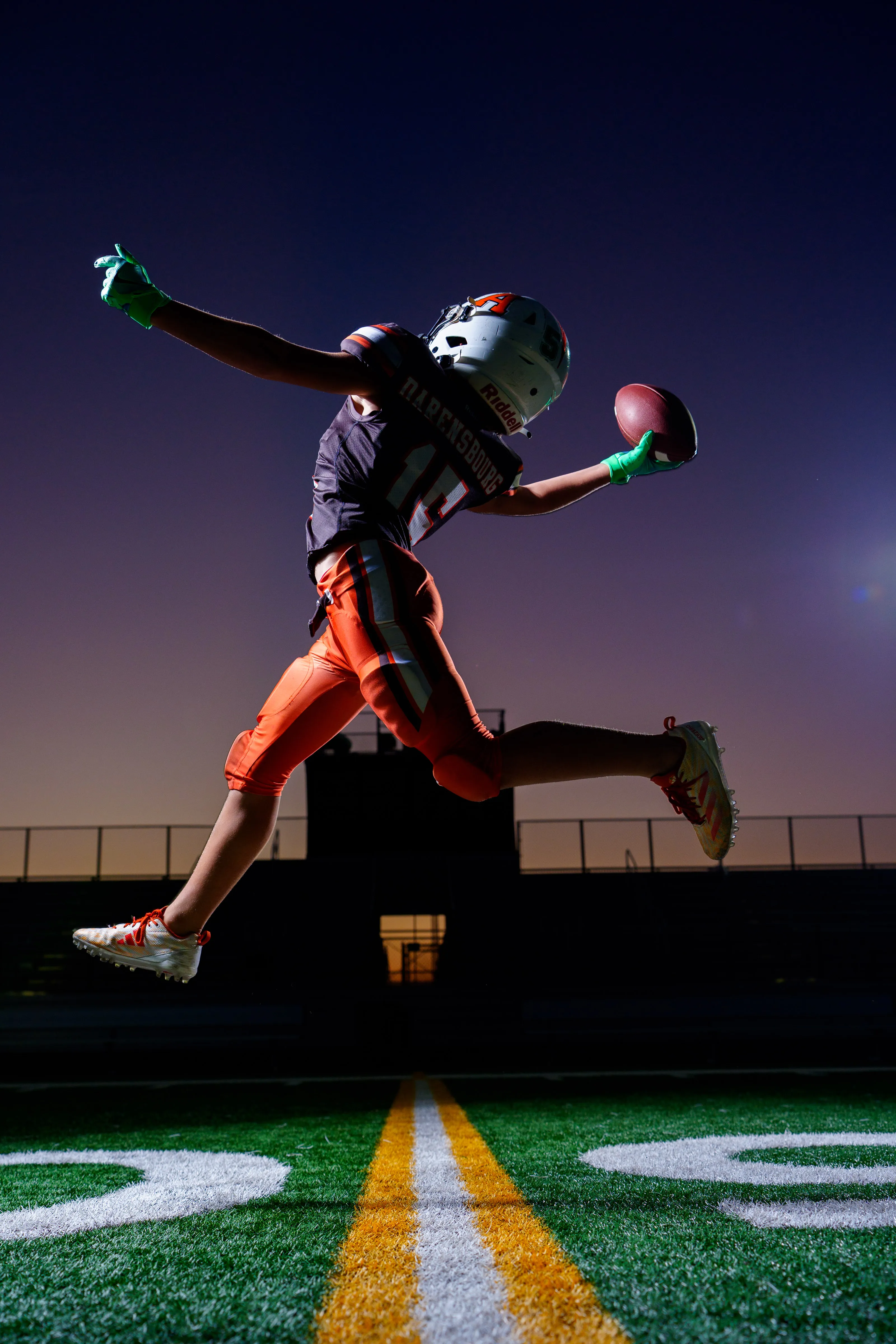 Football receiver leaping for a one-handed catch under stadium lights at night