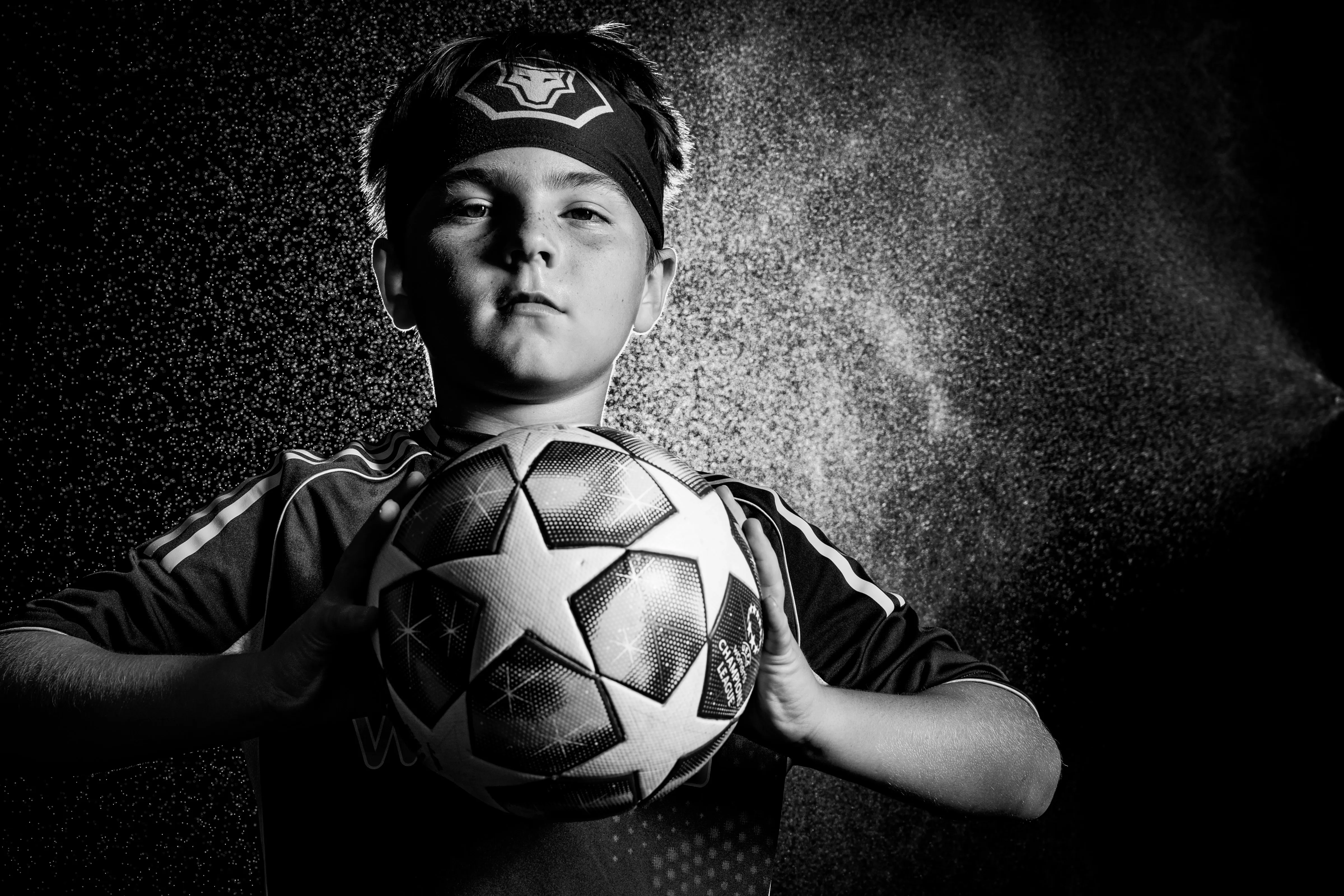 Black and white portrait of a soccer player holding out the ball in mist