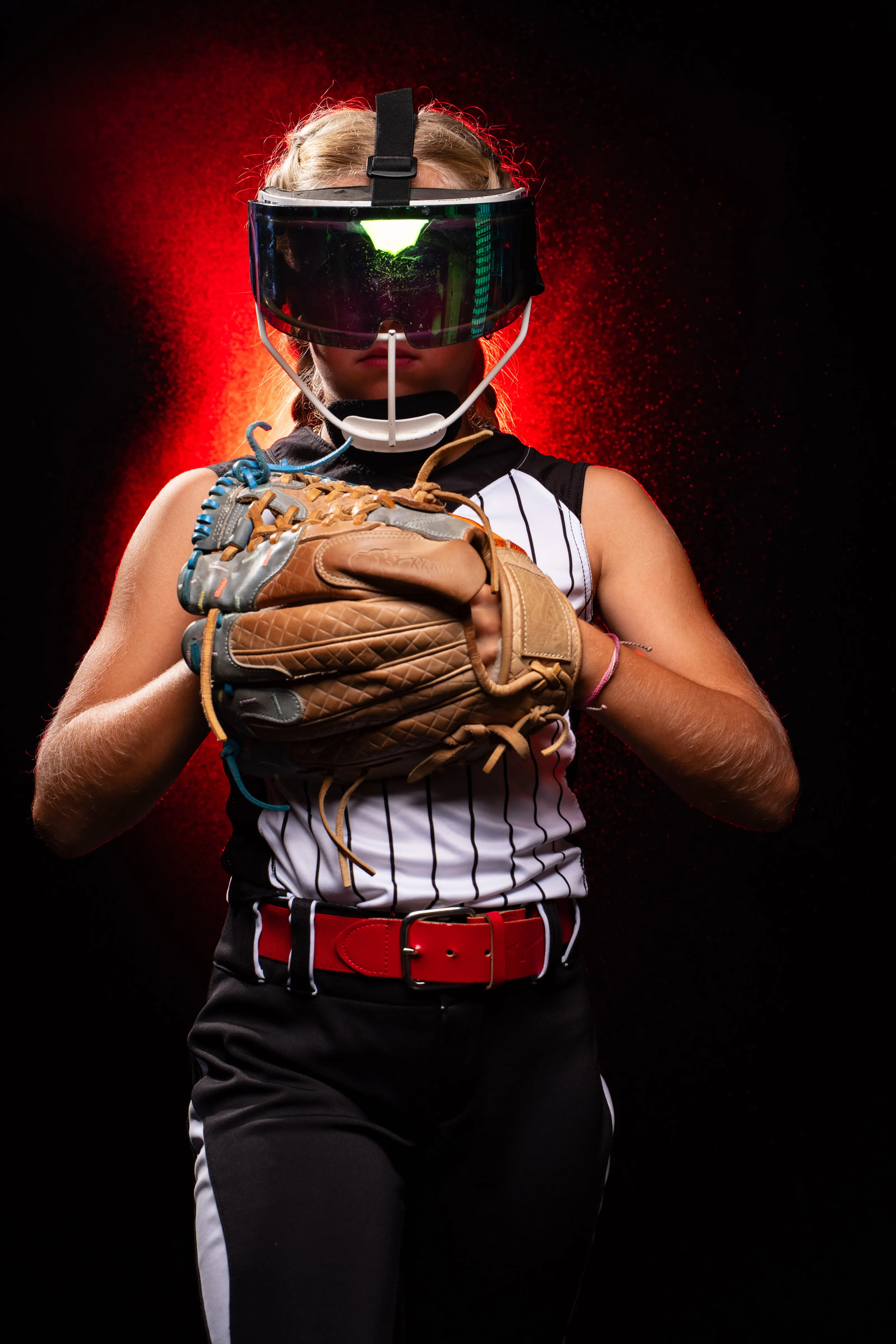 Softball catcher in gear with dramatic red rim lighting, studio sports portrait